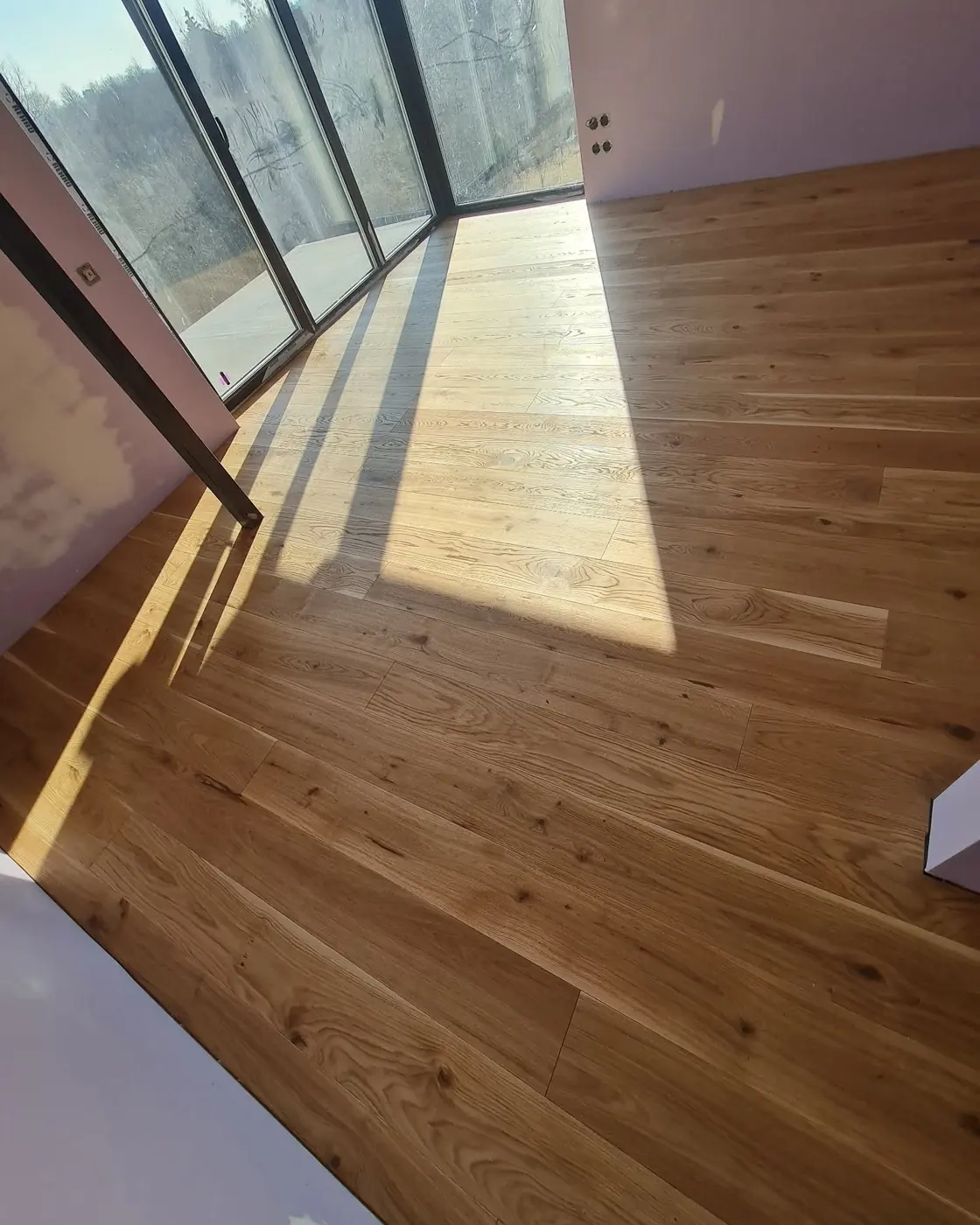 A finished oak floor in an empty room, sunlight falling across it in bands from the windows