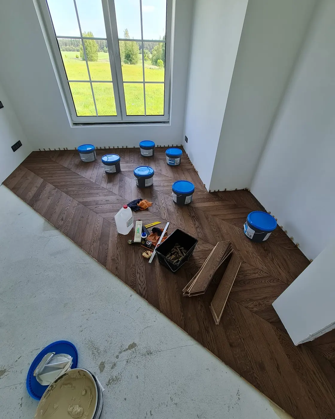 Buckets of Wakol MS 227 adhesive and an open one on site, on a half-laid oak chevron floor