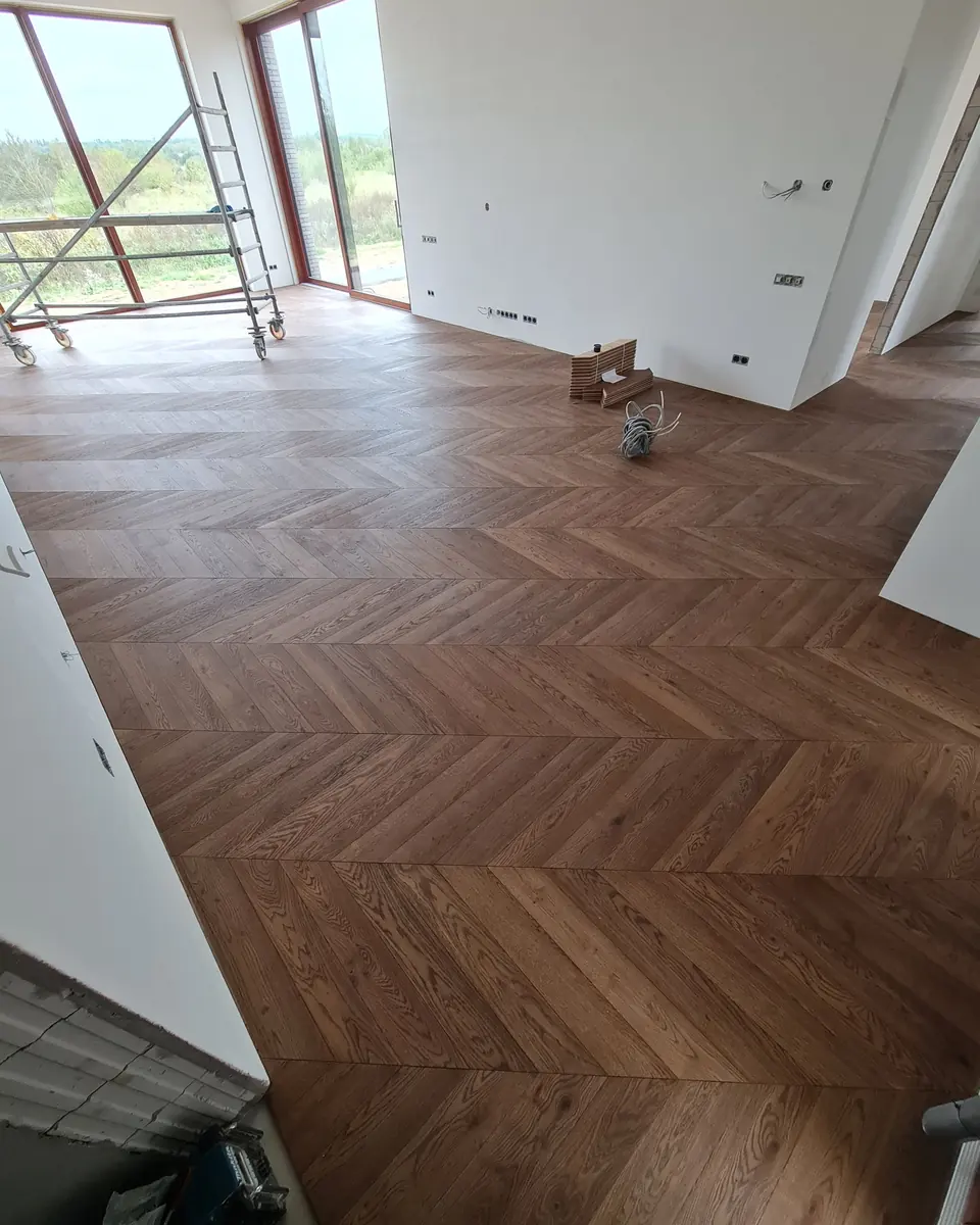 Oak chevron across a living room, a glazed wall onto the yard on the left, the house still at construction stage