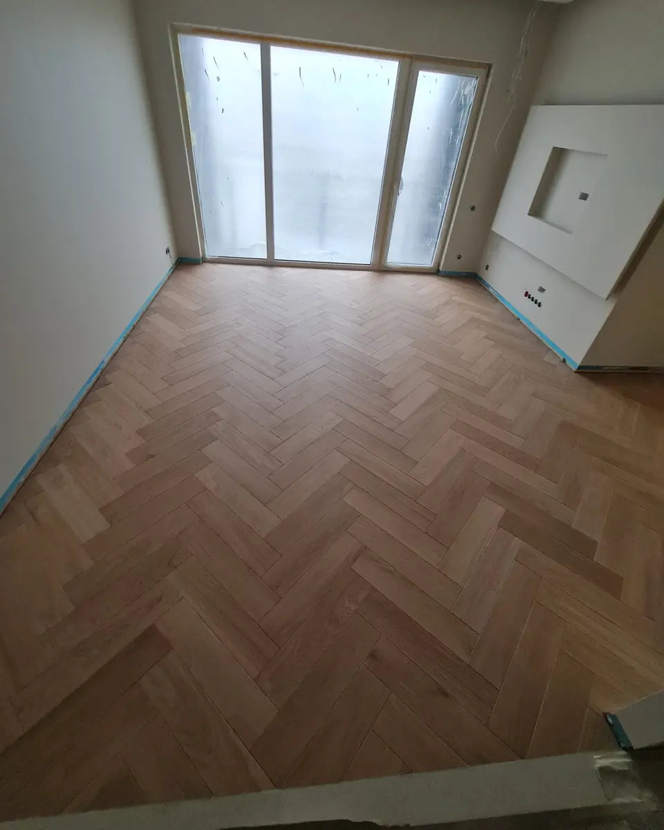 Pale oak classic herringbone by the window, the base of the walls still masked with tape