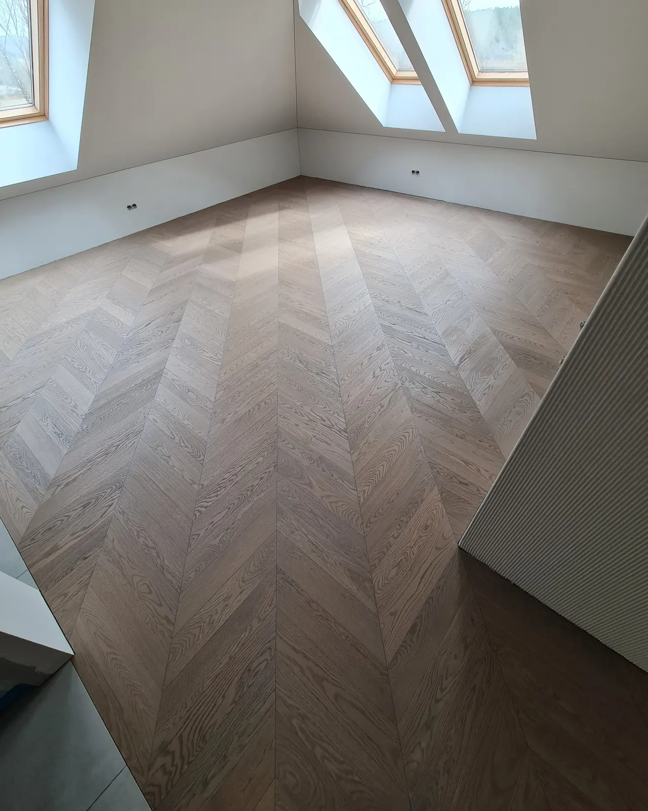 The finished oak chevron floor in the same attic room with its roof windows