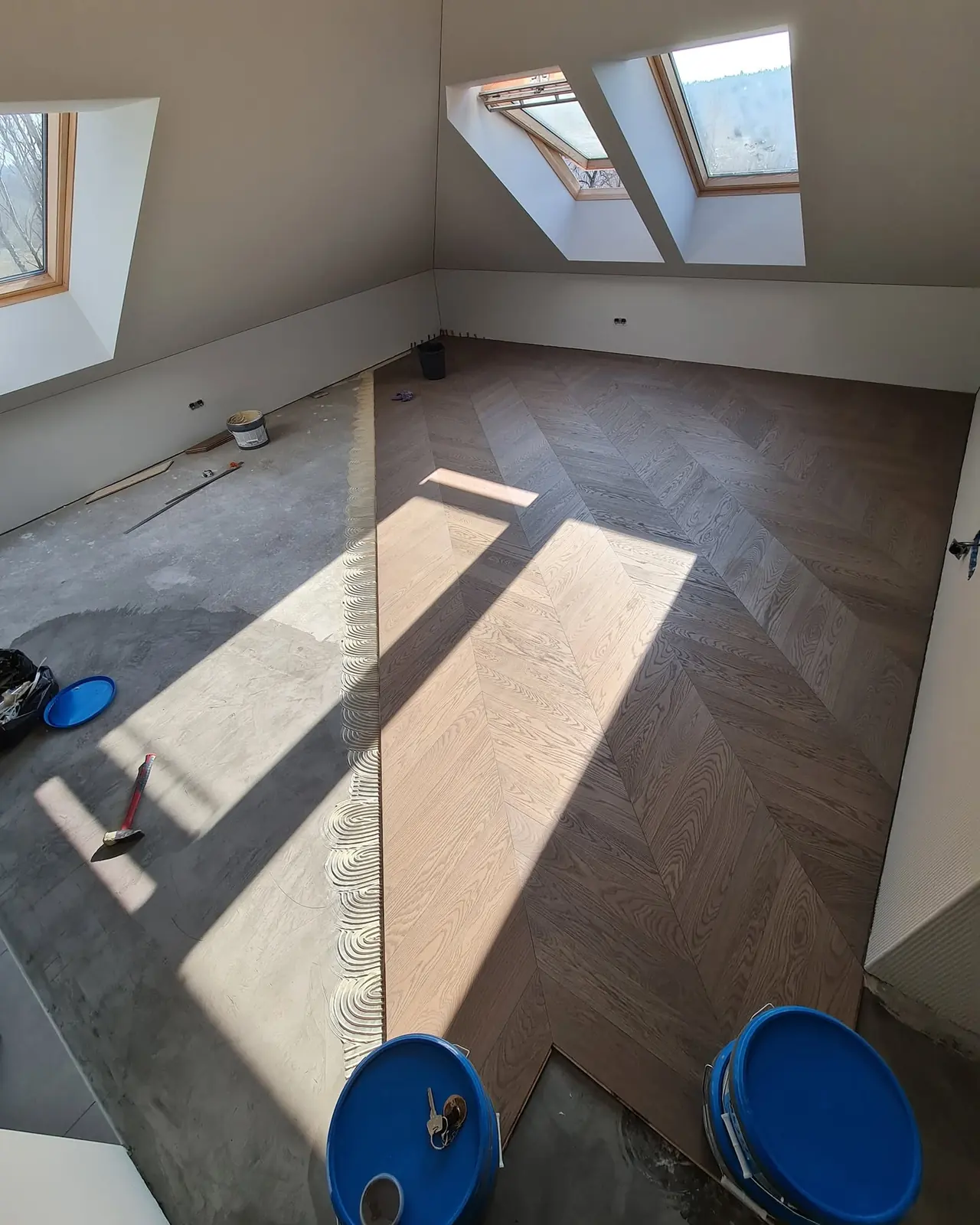 A levelled concrete substrate with a band of combed adhesive, the oak chevron already laid to the right